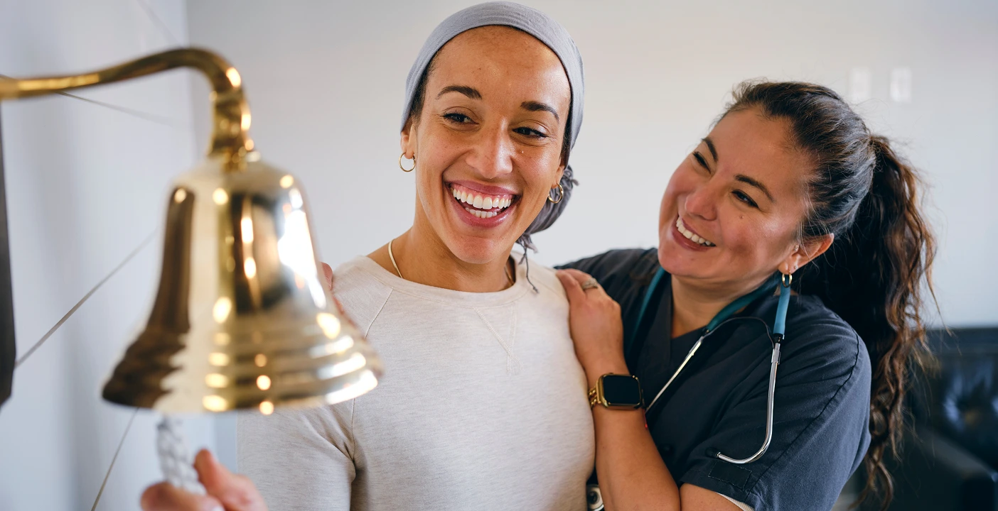 Patient rings bell, celebrating end of treatment and progress in cancer research, supported by a smiling healthcare worker.